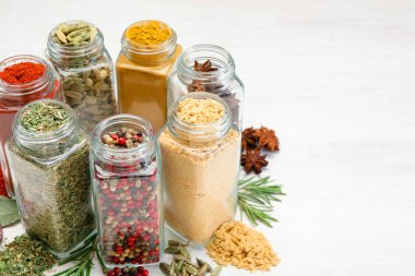 Beyaz masadaki kavanozlarda farklı aromatik baharatlar, yakın plan.