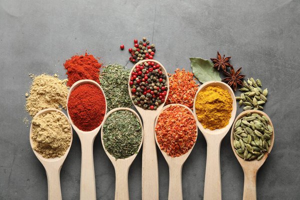 Много различных специй в ложках на сером столе, плоский лежал