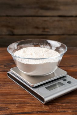 Elektronik mutfak terazisi ve ahşap masa üzerinde bir kase un.