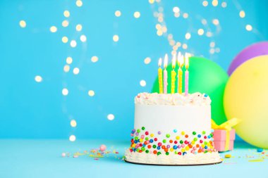 Renkli süslemeli nefis bento keki ve bulanık ışıklara karşı açık mavi masada yanan mumlar. Metin için boşluk