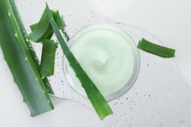 Aloe vera özütüyle nemlendirici krem, beyaz arka planda yapraklar ve ıslak ayna, düz bir zemin