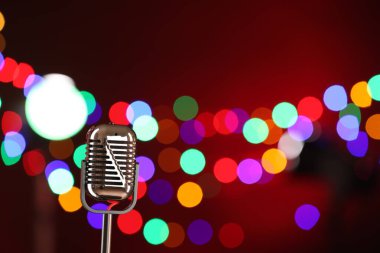 Koyu kırmızı arka planda, bulanık ışıkları olan klasik mikrofon, mesaj için yer. Müzik ekipmanları