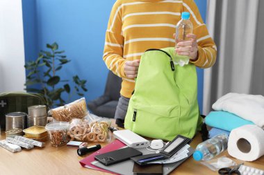 Hayatta kalma kiti. Kadın, ahşap masada sırt çantasına farklı acil durum malzemeleri yerleştiriyor.