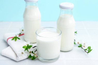 Taze süt ve çiçekler beyaz masada açık mavi arka planda