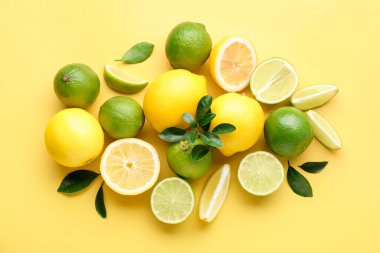 Sarı zemin üzerinde taze limon ve limon, düz uzanmış.