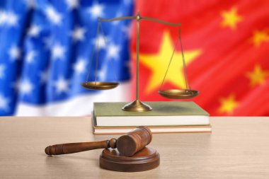 Yargıç tokmağı, adalet terazisi ve ahşap masa üzerinde ABD ve Çin bayraklarına karşı kitaplar.