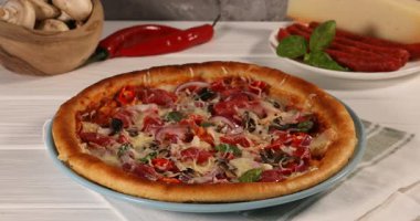 Beyaz ahşap masada ince füme sosisli pizza üzerine fesleğen ekleyen kadın.