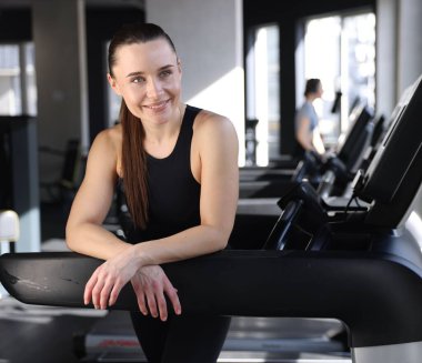 Spor salonunda koşu bandında gülümseyen kadının portresi.