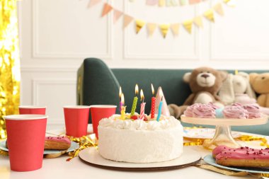İçi yanan mumlarla dolu lezzetli bir pasta ve masa içinde farklı ikramlar. Doğum günü sürpriz partisi