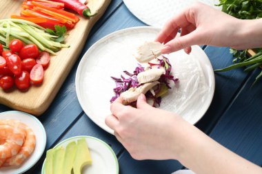 Mavi ahşap masada nefis börek yapan bir kadın.