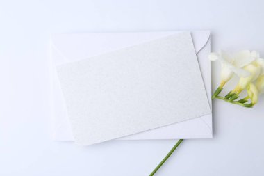 Boş tebrik kartı, beyaz arka planda kağıt zarf ve çiçek, düz uzanmış.
