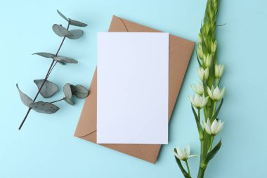 Boş tebrik kartı, kağıt zarf, ornithogalum çiçeği ve açık mavi arka planda okaliptüs dalı.