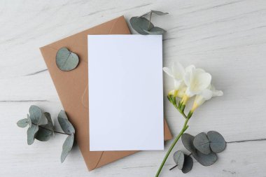 Boş tebrik kartı, frezya çiçeği ve okaliptüs dalları hafif ahşap zemin üzerinde, düz uzanmış