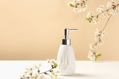 Bir şişe kozmetik ürünü ve bej arka planda beyaz masada güzel çiçekli dallar.