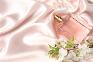 Bir şişe aromatik parfüm ve bej ipek kumaşlı güzel çiçekli dal, yakın plan. Metin için boşluk