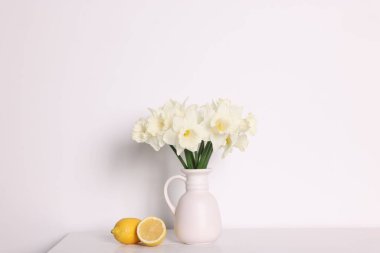 Vazodaki güzel nergisler ve beyaz ahşap masadaki limonlar