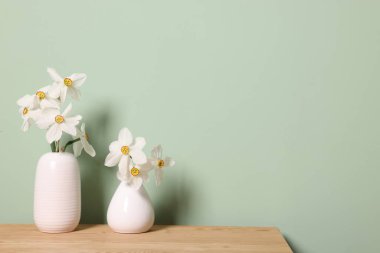 Açık yeşil duvarın yanındaki ahşap masadaki vazolardaki güzel nergisler. Metin için boşluk