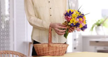 Bir kadın kapalı bir masada hasır sepete güzel çiçekler koyar, yakın plan.