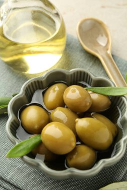 Lezzetli marine edilmiş zeytinler kasede, kaşıkta, yağda ve yeşil yapraklar masada, yakın plan.