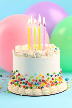 Renkli süslemeli nefis bento keki ve açık mavi masada yanan mumlar. Yakın plan.