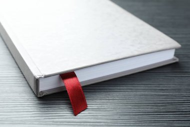 Siyah ahşap masa üzerinde kırmızı kurdele yer imi olan kitap, yakın plan.