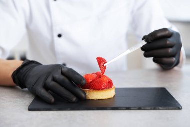 Şekerci, mutfaktaki gri masada çilekli lezzetli tart hazırlıyor, yakın plan.