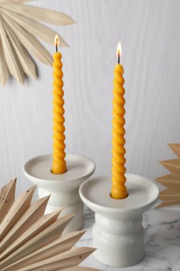 Balmumu mumları beyaz mermer masa ve kuru palmiye yaprakları üzerinde şamdanlarda yakıyor.