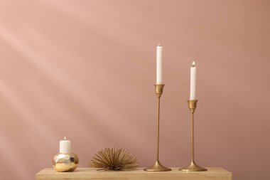 Mumları yanan şamdanlar ve kapalı alandaki açık kahverengi duvarın yanındaki ahşap dolapta dekor.