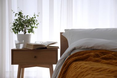 Yatağın yanında kitap, çiçek, bir bardak su ve bardaklar olan komodin.