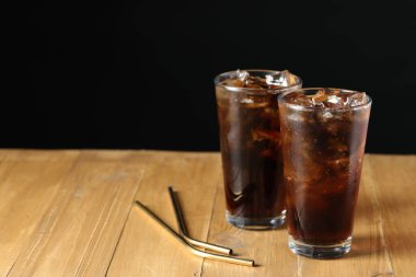 Kola bardaklarda buz ve tahta masada pipetle siyah arkaplanı yeniliyor, yakın plan. Metin için boşluk