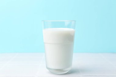 Açık mavi arka planda beyaz fayanslı bir bardak taze süt.