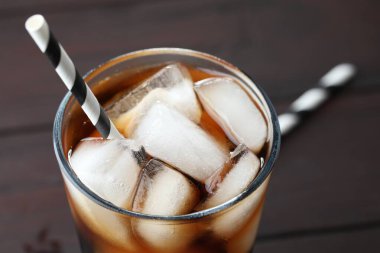 Kola buz küpleriyle tazeleniyor ve bulanık arkaplanda bardakta pipet, yakın plan