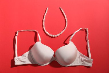 Kırmızı arka planda bej sütyen ve inci kolye.