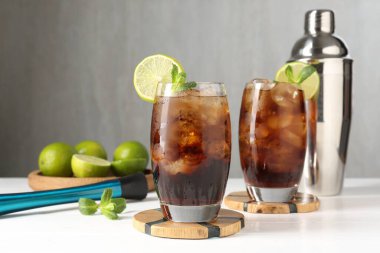 Lezzetli Küba Libre kokteyli, bardaklar, malzemeler, karıştırıcı ve sallanan beyaz tahta masa.