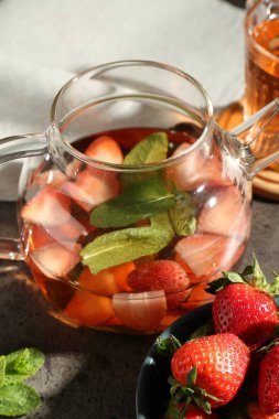 Gri masada aromatik meyve çayı, çilek ve nane içeren cam çaydanlık, yakın plan.