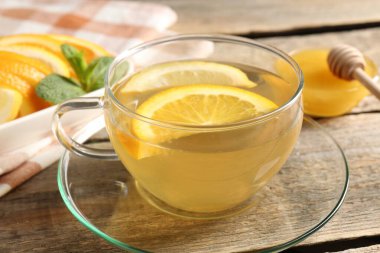 Cam fincanda aromatik meyve çayı, portakal, limon, bal ve nane, ahşap masada, yakın plan.