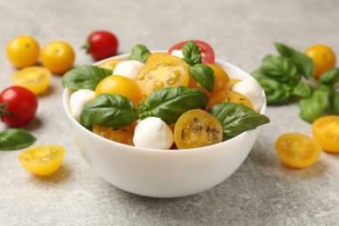 Sarı domatesli taze salata, fesleğen ve mozzarella peyniri gri masada, yakın plan.