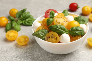 Sarı domatesli taze salata, fesleğen ve mozzarella peyniri gri masada, yakın plan.