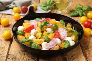 Sarı domatesli lezzetli salata, fesleğen, soğan ve ahşap masada mozzarella peyniri, yakın plan.