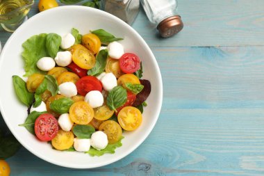 Sarı domatesli lezzetli salata, fesleğen ve mozzarella peyniri açık mavi ahşap masa, düz yatak. Metin için boşluk