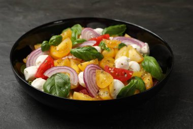 Sarı domatesli lezzetli salata, fesleğen, soğan ve siyah masada mozzarella peyniri, yakın plan.
