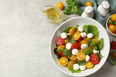 Sarı domatesli lezzetli salata, fesleğen ve açık gri masada mozzarella peyniri. Metin için boşluk