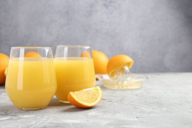 Portakal suyu bardakta, taze meyve suyu ve meyve sıkacağı gri masada, yakın plan. Metin için boşluk