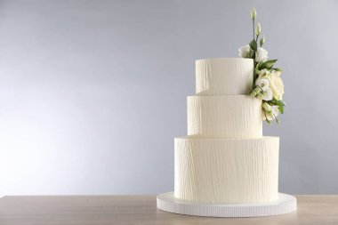 Gri arka planda, ahşap masada çiçeklerle süslenmiş lezzetli düğün pastası. Metin için boşluk