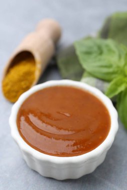 Lezzetli köri sosu, toz ve fesleğen yaprakları gri masada, yakın plan.