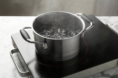 Kaynar suyla pişirme tenceresi ve beyaz mermer masa üzerinde gri arka plan, yakın çekim