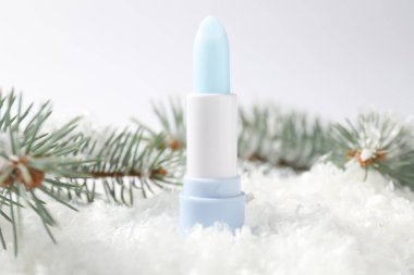 Nemlendirici dudak kremi ve suni kar üzerindeki köknar ağacı dalları beyaz arka planda, yakın plan. Kış bakımı