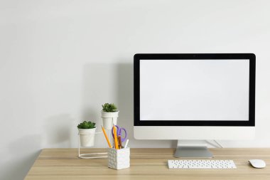 Bilgisayar, klavye, fare, farklı kırtasiye malzemeleri ve ahşap ofis masasındaki çiçek dekoru beyaz arka planda