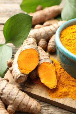 Zerdeçal tozu, kökler ve yapraklar ahşap masada, yakın plan.