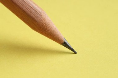Sarı arka planda keskin bir grafit kalem, yakın plan.